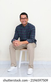 Asian Man Sitting In A Bench While Smiling To The Camera