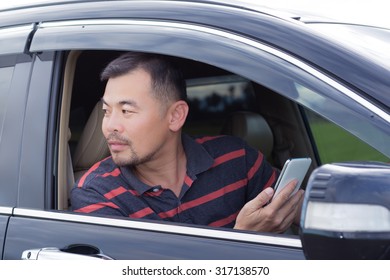 Asian Man Sitting In Car Holding Mobile Phone And Looking Back