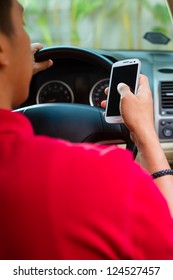 Asian Man Sitting In Car With Mobile Phone In Hand Texting While Driving