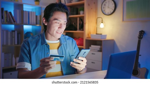 Asian Man Sitting On The Floor Is Holding Credit Card And Mobile Phone For Shopping Online By Laptop At Home