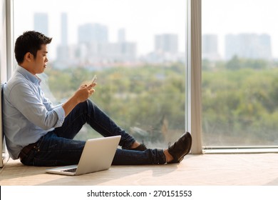 Asian Man Sitting At The Window And Text Messaging