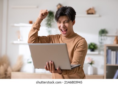 An Asian Man Is Smiling And Expressing Happy Feelings On The Computer Laptop Screen. The Young Male Got Good News And Show His Cheerful Face. 