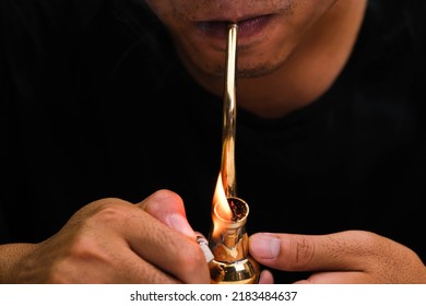 Asian Man Smokes Marijuana From A Pipe At Home. Studio Shoot With Model Simulating Smoking Pot With A Pipe In A Dark Background. Cannabis Legalisation.