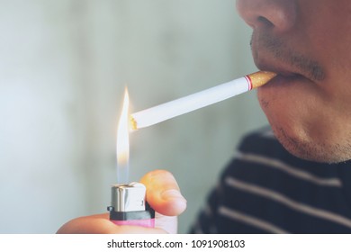 asian man smoking a cigarette. using lighter flame burn cigarette smoke spread. Dark background.	