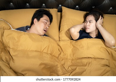 Asian Man Snoring With Open Mouth,wife Is Closing Ears With Hands,stressed By Loud Noise,annoying Snoring Of Husband,risk Of Sleep Apnea While Sleeping,unhappy Woman Wakes Up While Lying In The Bed