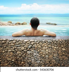 Asian Man Soaking In Outdoor Pool With Sky.