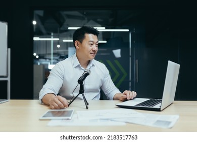 An Asian Man Speaking Into A Laptop Camera Into A Microphone, Holding A Conference, Recording A Video Call, Conducting A Webinar, Listening To A Podcast, Gesturing With His Hands, Smiling.