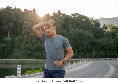 An Asian man in sportswear is feeling tired after a long run on a sunny day. exhausted, fatigue, intense workout - Powered by Shutterstock