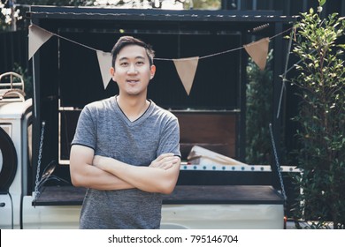 Asian man standing with arms folded in front of food truck. Business owner with arms crossed smiling with own food stall vehicle - Powered by Shutterstock