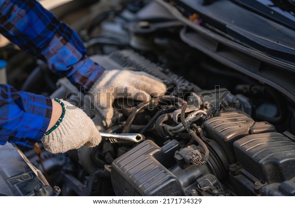 Asian man standing in front of inspection vehicle\
and inspecting machinery Problems in the car engine in the house\
and found problems inside the car to repair. Asian man maintains a\
car\'s engine