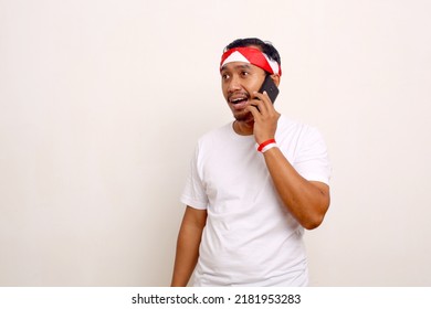 Asian Man Standing With Indonesian Attribute While Talking On Phone. Independence Day Concept