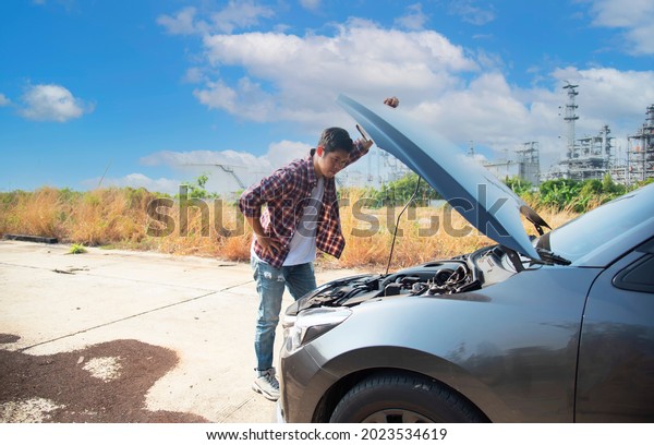Asian man stands in\
front of car checking car condition after a broken car. Broken car\
down on the road.\
