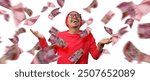 Asian man stands with Indonesian Rupiah banknotes flying around him, creating a money shower effect against a white background. Concept of financial success, prosperity, and Indonesia Independence Day