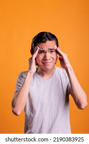 Asian Man Suffering From Headache, Touching Temples With Fingers, Looking At Camera. Exhausted Teenager Having Migraine, Overworked Stressed Young Person Feeling Unwell, Mid Shot