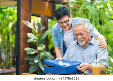 Asian man surprised elderly father with Birthday gift at outdoor cafe restaurant on summer holiday vacation. Family relationship, celebrating father's day and senior people health care concept. - Powered by Shutterstock