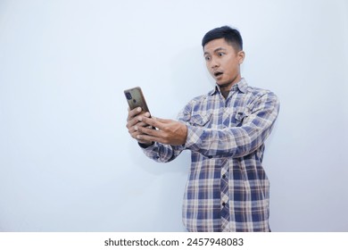 asian man surprised looking at smartphone. expressive face looking at something. men wear plaid shirts. - Powered by Shutterstock