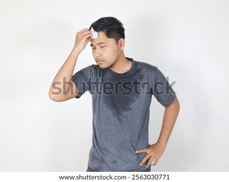 Asian man sweating while wiping sweat from his forehead with a tissue with a face that looks uncomfortable