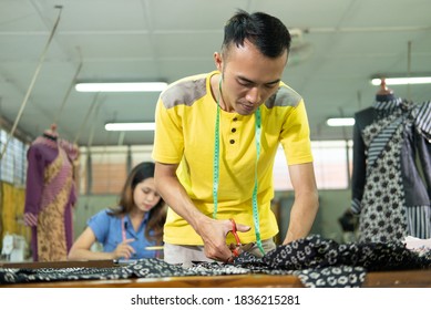 Asian Man Tailor Standing When Cutting A Cloth Pattern Using Scissor At The Clothing Production Room