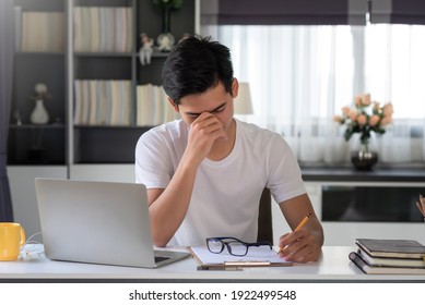 Asian Man Are Tired And Stressed About Working On A Laptop And Taking Notes At Home.