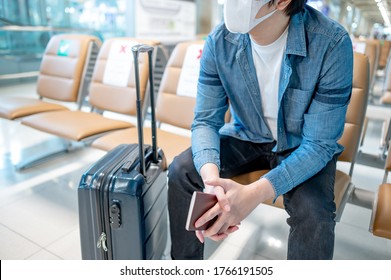 Asian man tourist wearing protective face mask sitting with suitcase luggage in airport terminal. Coronavirus (COVID-19) pandemic prevention when travel abroad. Health awareness and social distancing