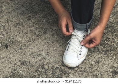 Asian Man Tying Shoe Laces On The Ground 