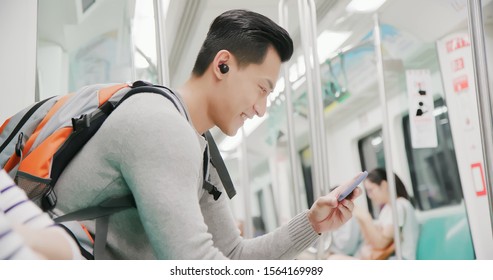 asian man use wireless earbuds to watch video on the subway