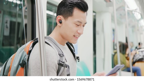 asian man use wireless earbuds to listen music or watch video on the metro