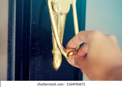 Asian Man Uses His Right Hand To Knock The Door By Using A Golden Door Knocker.