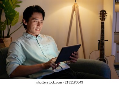 Asian Man Is Using Digital Tablet At Night In Living Room