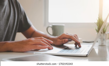 Asiatischer Mann mit Laptop zu Hause beim Sitzen auf dem Holztisch.Männliche Hände tippen auf der Notebook-Tastatur. Online-Ausbildung und freiberufliche Tätigkeit. Computer, Laptop und Lernen remote.