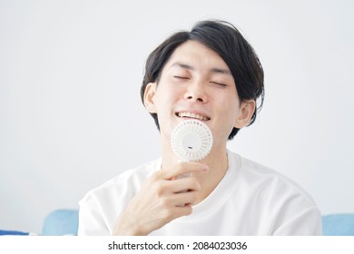 Asian Man Using A Portable Fan At Home