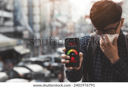 Asian man using a smartphone scanning the weather over smog city from PM2.5 dust. View of buildings with bad weather from Fine Particulate Matter.City air pollution and Unhealthy concept.pm2.5