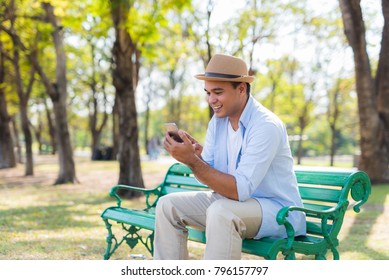asian man using smartphone while sitting in park