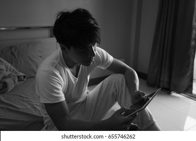 Asian man using tablet with sad mood in the room, sadness portrait concept, black and white tone.