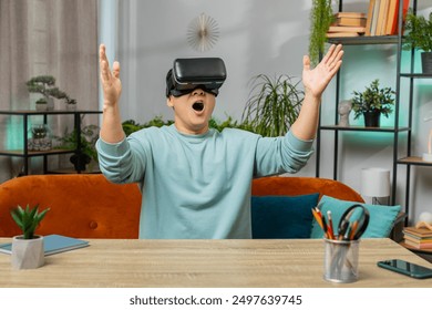 Asian man using virtual reality futuristic technology VR app headset helmet typing on virtual keyboard, play simulation 3D 360 online video game at home apartment. Guy in goggles sitting on sofa - Powered by Shutterstock