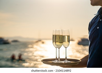 Asian man waiter holding champagne glass on the tray serving to group of passenger tourist travel on luxury catamaran boat yacht sailing in the ocean at summer sunset on beach holiday vacation trip. - Powered by Shutterstock