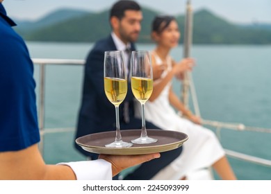 Asian man waiter serving champagne to passenger tourist while private catamaran boat yacht sailing in the ocean. Happy couple enjoy luxury outdoor lifestyle travel on summer beach holiday vacation. - Powered by Shutterstock