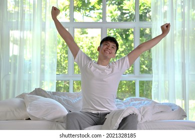 Asian man waking up in the morning sitting on bed and stretching