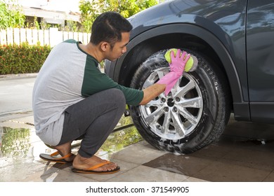 Asian Man Washing Car's Alloy Wheels On A Car Wash. Cleaning Concept.