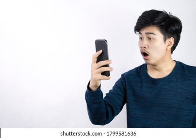 Asian Man Watching A Mobile Phone Poses With Excitement And Gasp On A Blank Background.