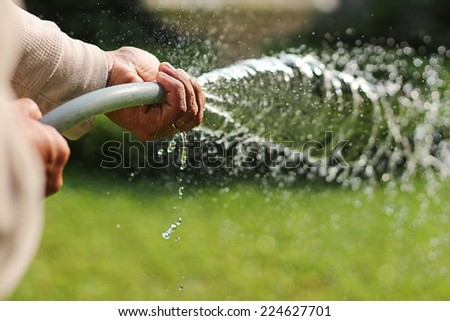 A asian man watering grass in the garden  in summer.