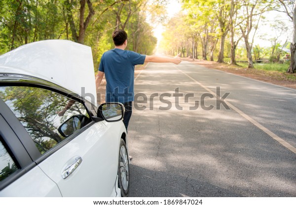 An Asian man is waving and signaling a hand for\
help. Because his car is\
broken