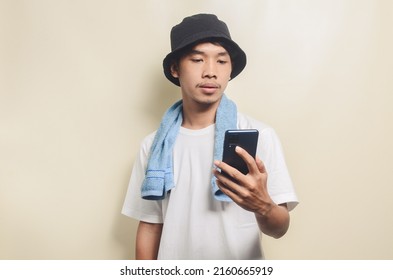 Asian Man Wearing Bright White T-shirt In Black Hat With Blue Towel Carrying Phone On Isolated Background