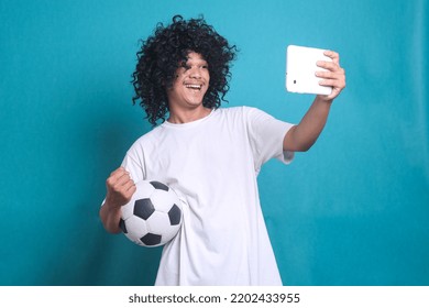 Asian Man Wearing Curly Hair Wig Cheer Up Supporting Football Sport Team While Holding Mobile Phone To Watch Soccer Ball Tv Live Stream