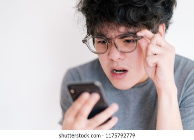 Asian man wearing eyeglasses obsessed with his smartphone isolated on a white background. Cause of nomophobia, shortsighted, nearsighted, longsighted, farsighted, astigmatic and other eye problem.