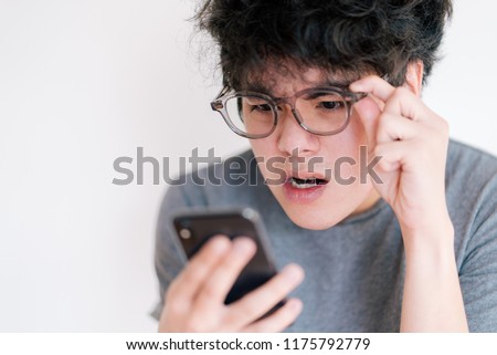 Asian man wearing eyeglasses obsessed with his smartphone isolated on a white background. Cause of nomophobia, shortsighted, nearsighted, longsighted, farsighted, astigmatic and other eye problem.