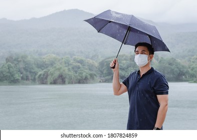 Asian man wearing face mask and holding umbrella to protect from get sick and wet when raining in monsoon season.  - Powered by Shutterstock