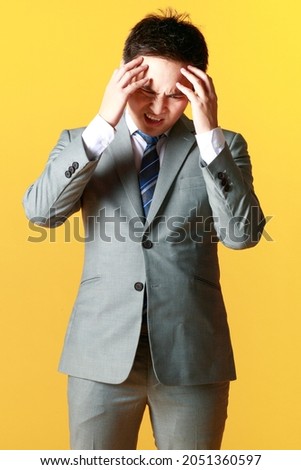 Asian man wearing gray suit hand held forehead standing thinking, stressing dismal failure
fearful and gestures in yellow background. Concept tense serious dissatisfied