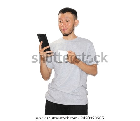 Asian man wearing gray t-shirt. left hand holding a cellphone, right hand holding a white mug. smiling expression. isolated white background            Stock photo © 