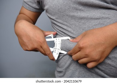 asian man wearing grey shirt checking his fat belly with calipers